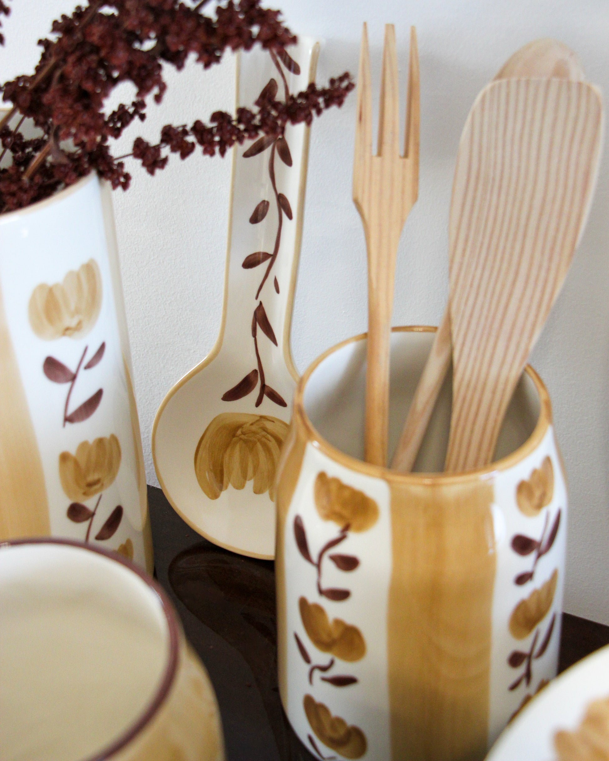 Decorative ceramic utensil holder with wooden utensils and floral patterns.