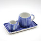 Two blue and white striped ceramic cups with matching saucers on a tray against a white background