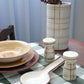 Dining table setting with ceramic plates, bowls, and a vase on a checkered tablecloth.