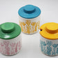 Three ceramic jars with floral patterns and colorful lids on a white background