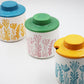 Three ceramic containers with colorful lids and floral patterns on a white background