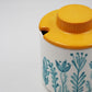 Container with a yellow lid and blue floral design on a white background
