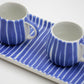 Two ceramic cups with blue and white striped design on a matching tray.