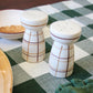 Two ceramic salt and pepper shakers on a checkered tablecloth.
