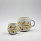 Two ceramic mugs with leaf patterns on a white background