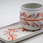 Ceramic cup with colorful leaf patterns on a matching tray against a white background