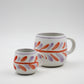 Two ceramic mugs with colorful feather patterns on a white background