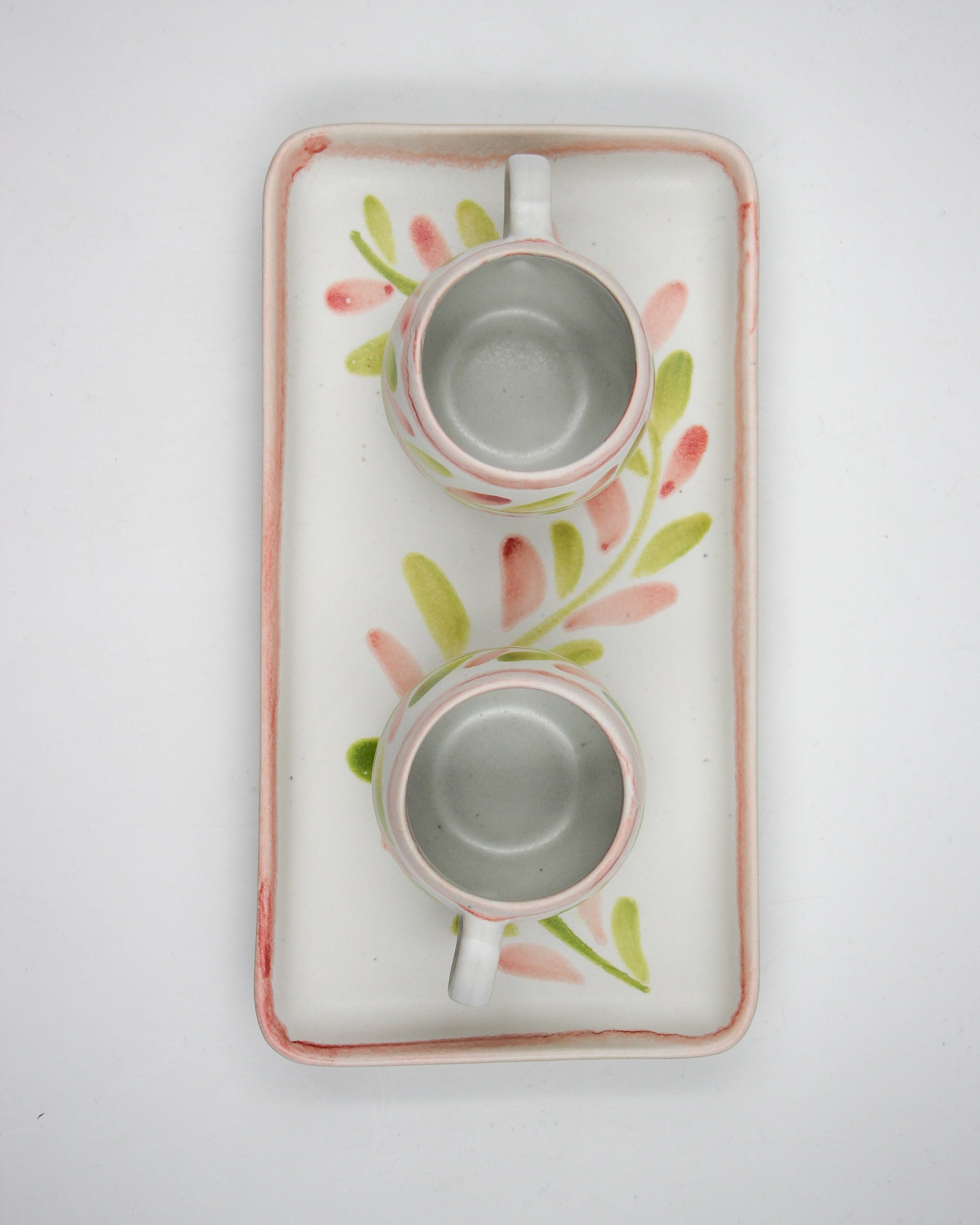 Two ceramic cups on a decorative tray with floral patterns on a light gray background