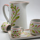 Ceramic pitcher, cups, and tray with floral patterns on a light gray background