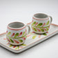Two ceramic mugs with floral patterns on a matching tray against a white background